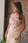 Woman wearing a floral dress standing against a brick wall.